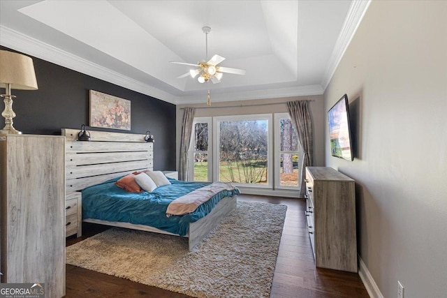 bedroom featuring dark wood-style floors, a raised ceiling, ornamental molding, a ceiling fan, and baseboards