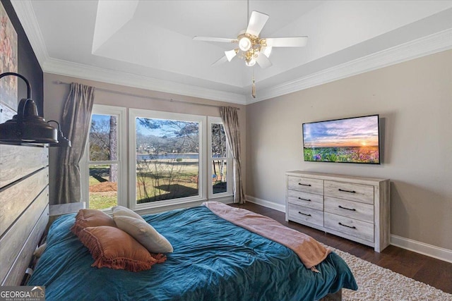 bedroom with baseboards, a raised ceiling, a ceiling fan, dark wood-type flooring, and crown molding