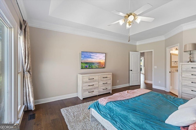 bedroom featuring baseboards, wood finished floors, ensuite bathroom, a tray ceiling, and crown molding