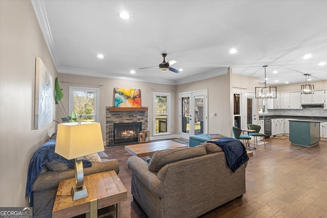 living room with recessed lighting, dark wood finished floors, ornamental molding, a fireplace, and ceiling fan with notable chandelier