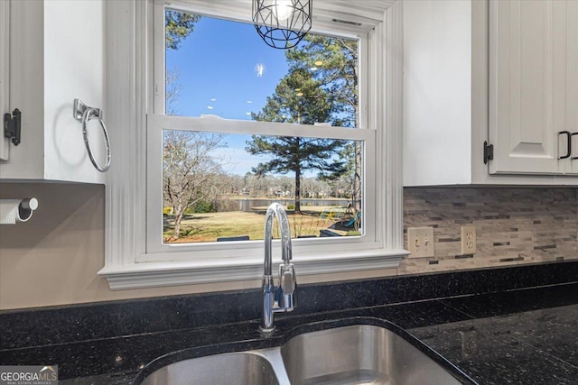 kitchen featuring dark stone counters, backsplash, a sink, and white cabinets