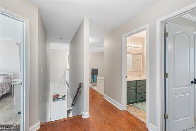 hallway with light wood finished floors, baseboards, and an upstairs landing