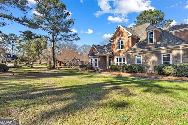 view of front of house featuring a front yard, brick siding, and roof with shingles