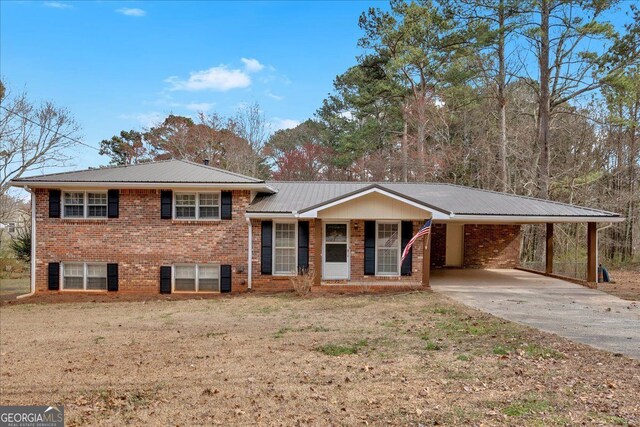 tri-level home featuring metal roof, brick siding, driveway, a carport, and a front yard