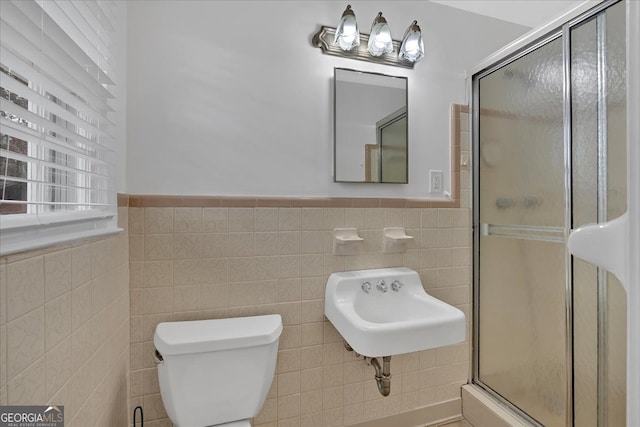 bathroom with wainscoting, a shower stall, toilet, and tile walls