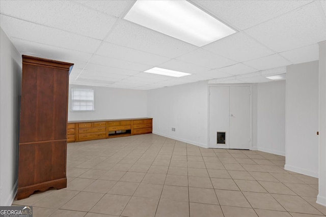 below grade area featuring light tile patterned floors, a drop ceiling, and baseboards