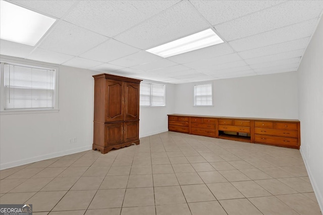 basement featuring a drop ceiling, light tile patterned flooring, and baseboards