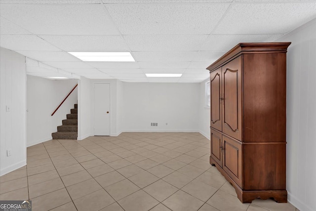 finished basement featuring a paneled ceiling, light tile patterned floors, stairs, and visible vents