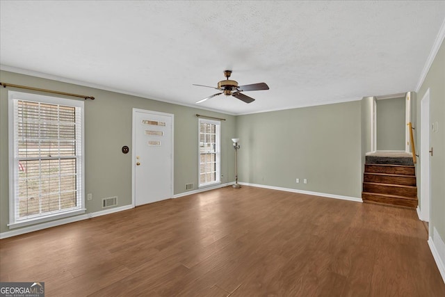 unfurnished living room featuring visible vents, baseboards, stairway, wood finished floors, and crown molding