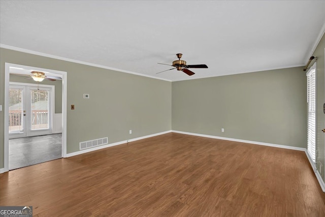 unfurnished room with a ceiling fan, visible vents, wood finished floors, and ornamental molding