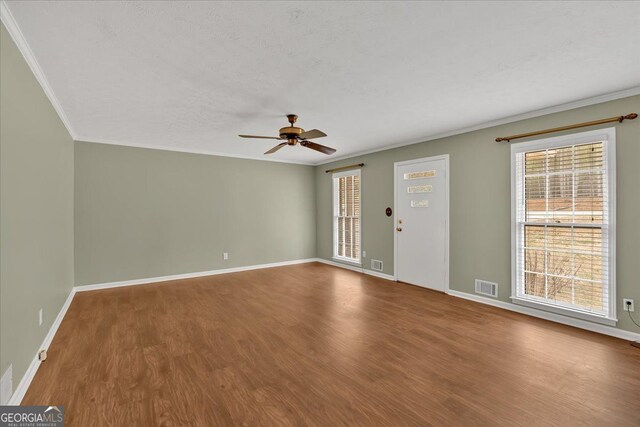 spare room with baseboards, visible vents, wood finished floors, and ornamental molding