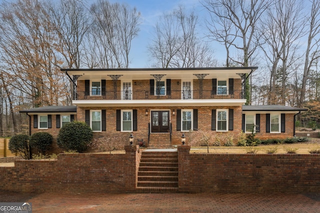 view of front of property featuring a balcony, french doors, and brick siding