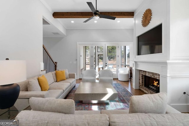 living area with wood finished floors, a lit fireplace, stairs, beam ceiling, and recessed lighting