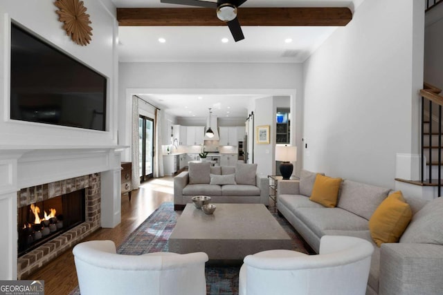 living area with beam ceiling, recessed lighting, a brick fireplace, ceiling fan, and wood finished floors