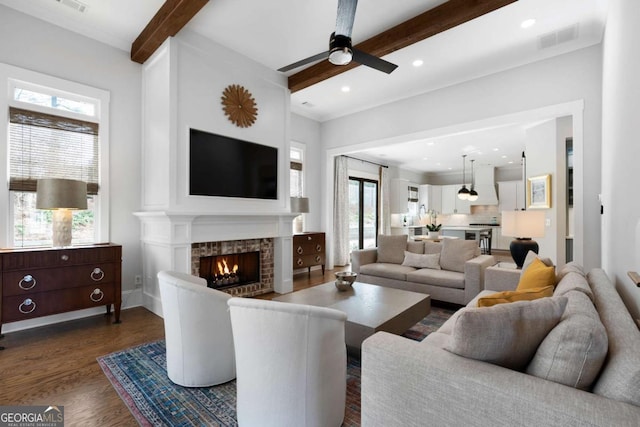 living room featuring a lit fireplace, beam ceiling, dark wood-type flooring, and visible vents