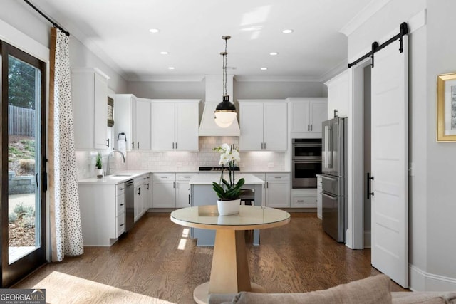 kitchen with a barn door, dark wood-style flooring, appliances with stainless steel finishes, custom exhaust hood, and decorative backsplash