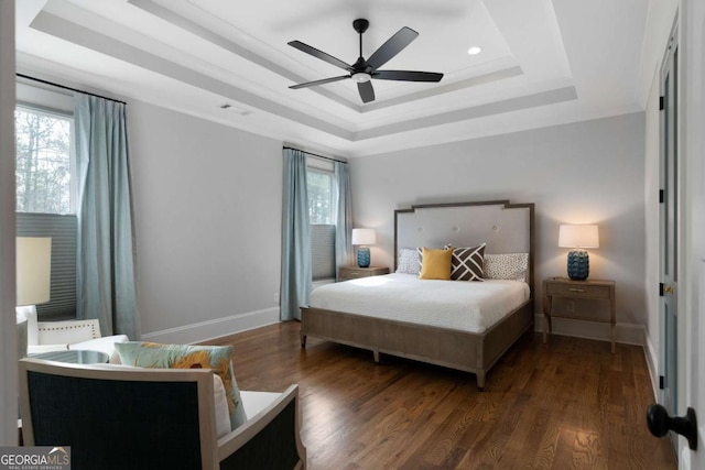 bedroom with a tray ceiling, wood finished floors, visible vents, and baseboards