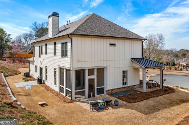 back of house with a chimney, a shingled roof, a sunroom, a standing seam roof, and cooling unit