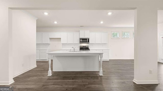 1039 Blue Juniper Cir, Loganville, GA 30052 - kitchen featuring stainless steel microwave, range, white cabinetry, dark wood finished floors, and a center island with sink
