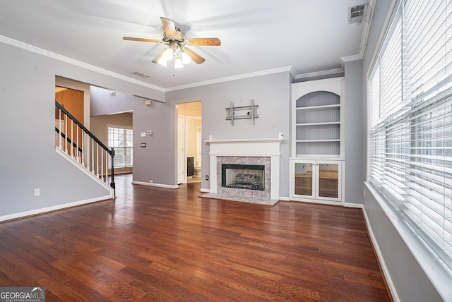 unfurnished living room with built in features, a fireplace with flush hearth, ornamental molding, wood finished floors, and baseboards