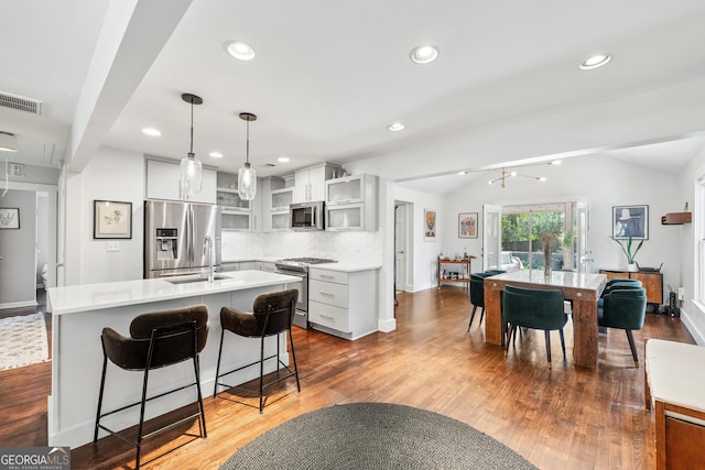 kitchen featuring visible vents, an island with sink, vaulted ceiling, appliances with stainless steel finishes, and open shelves