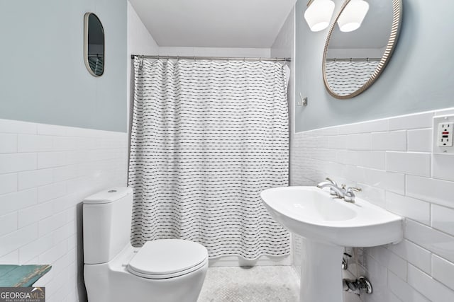 full bathroom with curtained shower, tile walls, toilet, and wainscoting