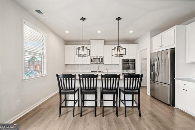 kitchen with light wood finished floors, appliances with stainless steel finishes, backsplash, and white cabinetry