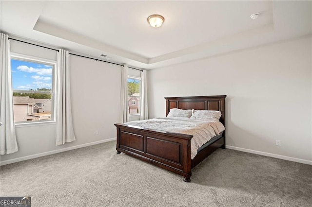 bedroom featuring a tray ceiling, light colored carpet, and baseboards