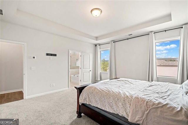 carpeted bedroom with baseboards, a raised ceiling, ensuite bathroom, and visible vents