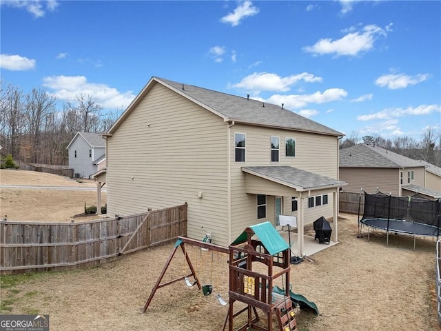 back of house with a trampoline, a fenced backyard, a playground, a patio, and a shingled roof