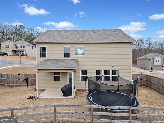 back of house with a fenced backyard, a trampoline, roof with shingles, and a patio