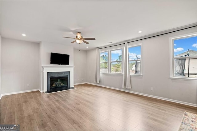 unfurnished living room with baseboards, a ceiling fan, a glass covered fireplace, and wood finished floors
