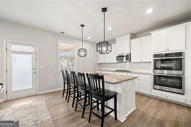 kitchen with light wood-style floors, appliances with stainless steel finishes, a kitchen breakfast bar, and a kitchen island with sink
