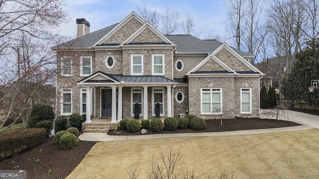 view of front facade with a chimney, metal roof, covered porch, a standing seam roof, and brick siding