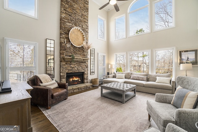 living room featuring dark wood-style floors, a ceiling fan, and a stone fireplace