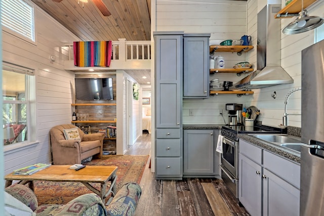 kitchen with stainless steel appliances, wood walls, wood ceiling, wall chimney range hood, and dark wood finished floors