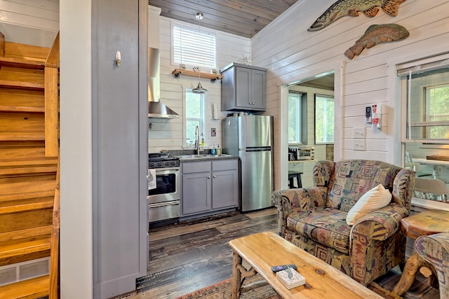 kitchen with appliances with stainless steel finishes, wood walls, dark wood finished floors, and gray cabinetry