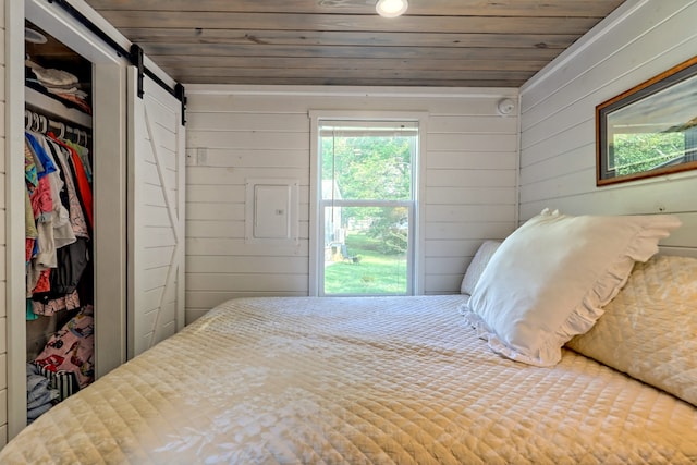 bedroom featuring a barn door, wood walls, wooden ceiling, and a closet