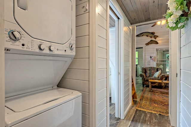 clothes washing area featuring laundry area, wood walls, wood finished floors, wood ceiling, and stacked washer and clothes dryer