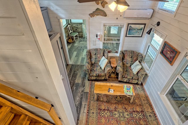 living room featuring wood walls, a wall unit AC, wood finished floors, and a ceiling fan