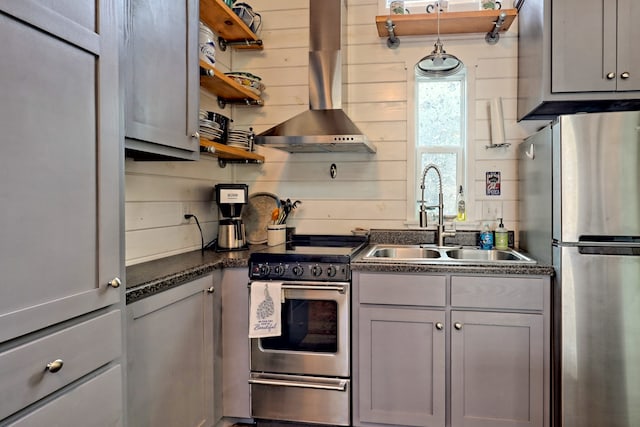 kitchen featuring stainless steel appliances, a sink, wall chimney exhaust hood, open shelves, and dark countertops