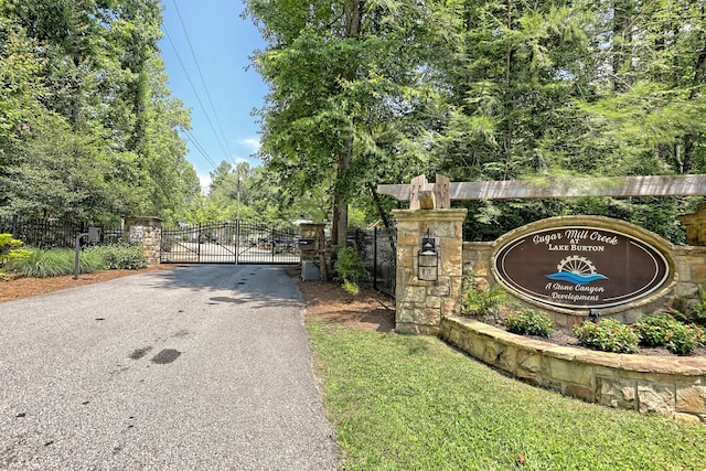 community / neighborhood sign featuring aphalt driveway, a gate, and fence