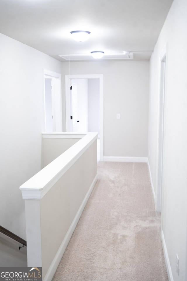 corridor with attic access, baseboards, light colored carpet, and an upstairs landing