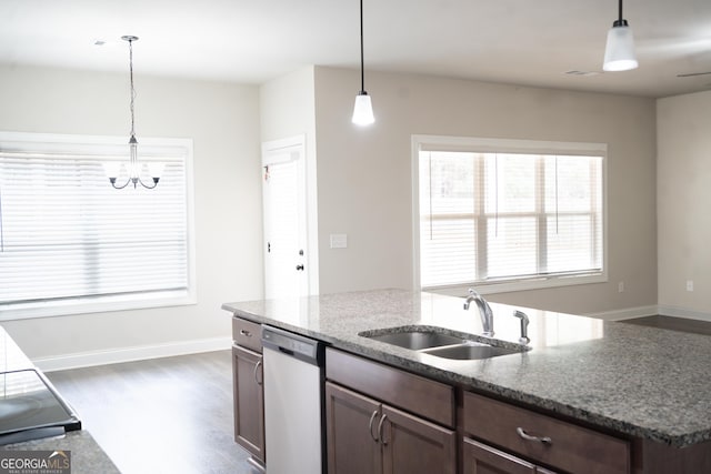 kitchen featuring dark wood-style floors, light stone counters, decorative light fixtures, stainless steel dishwasher, and a sink