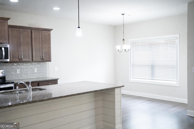 kitchen featuring a sink, dark wood-style floors, appliances with stainless steel finishes, decorative backsplash, and dark stone counters