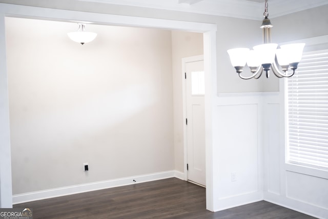 unfurnished dining area with baseboards, dark wood finished floors, a wainscoted wall, crown molding, and a notable chandelier