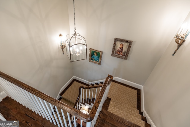 stairway featuring baseboards, an inviting chandelier, and wood finished floors