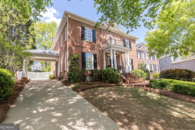 view of front facade with brick siding, fence, a balcony, a carport, and a gate