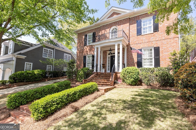 colonial inspired home with brick siding, a front yard, and a balcony