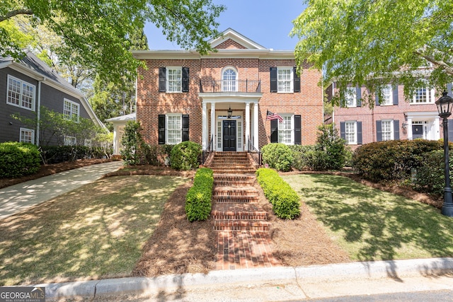 georgian-style home featuring a front lawn, brick siding, and a balcony